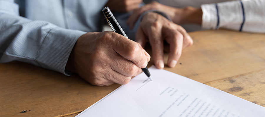 Hands of an older man signing estate planning documents with a black pen
